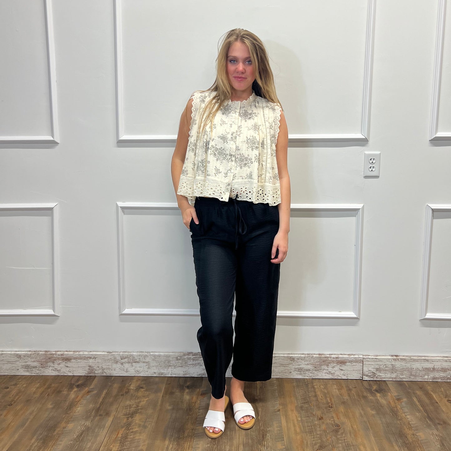 Woman standing in a room with a white paneled wall and wooden floor.
