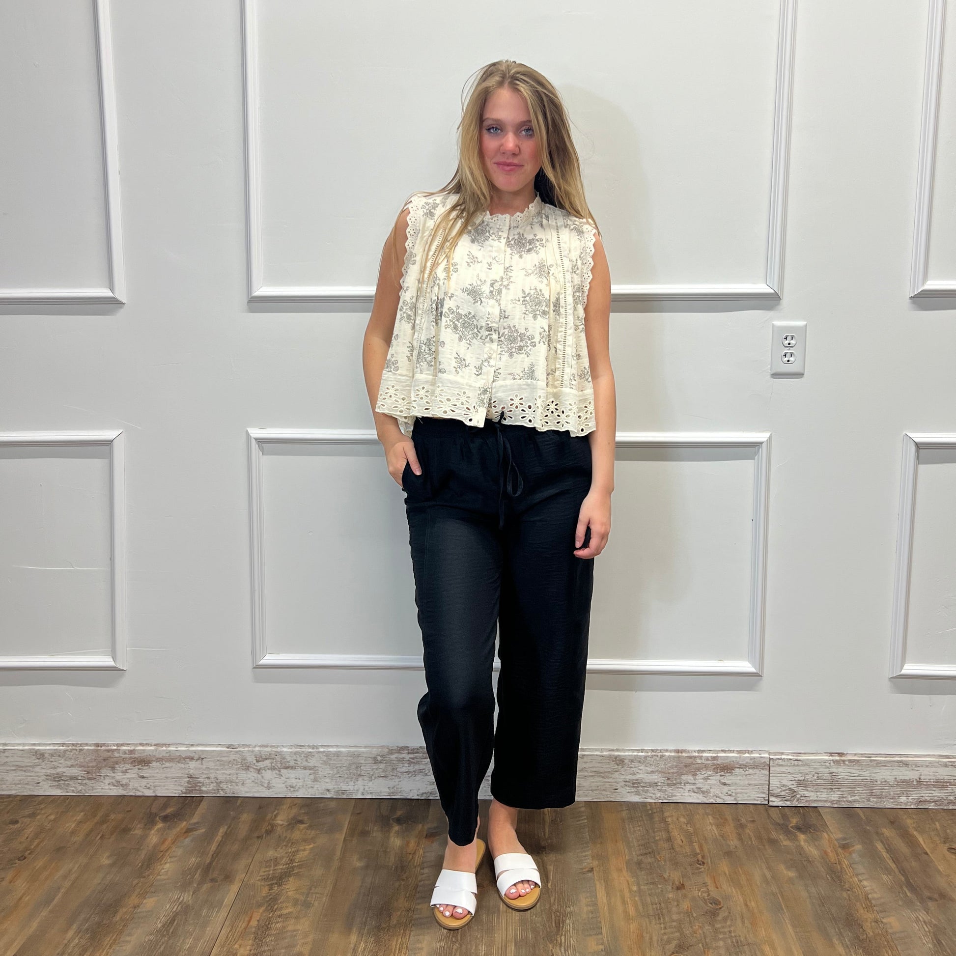 Woman standing in a room with a white paneled wall and wooden floor.