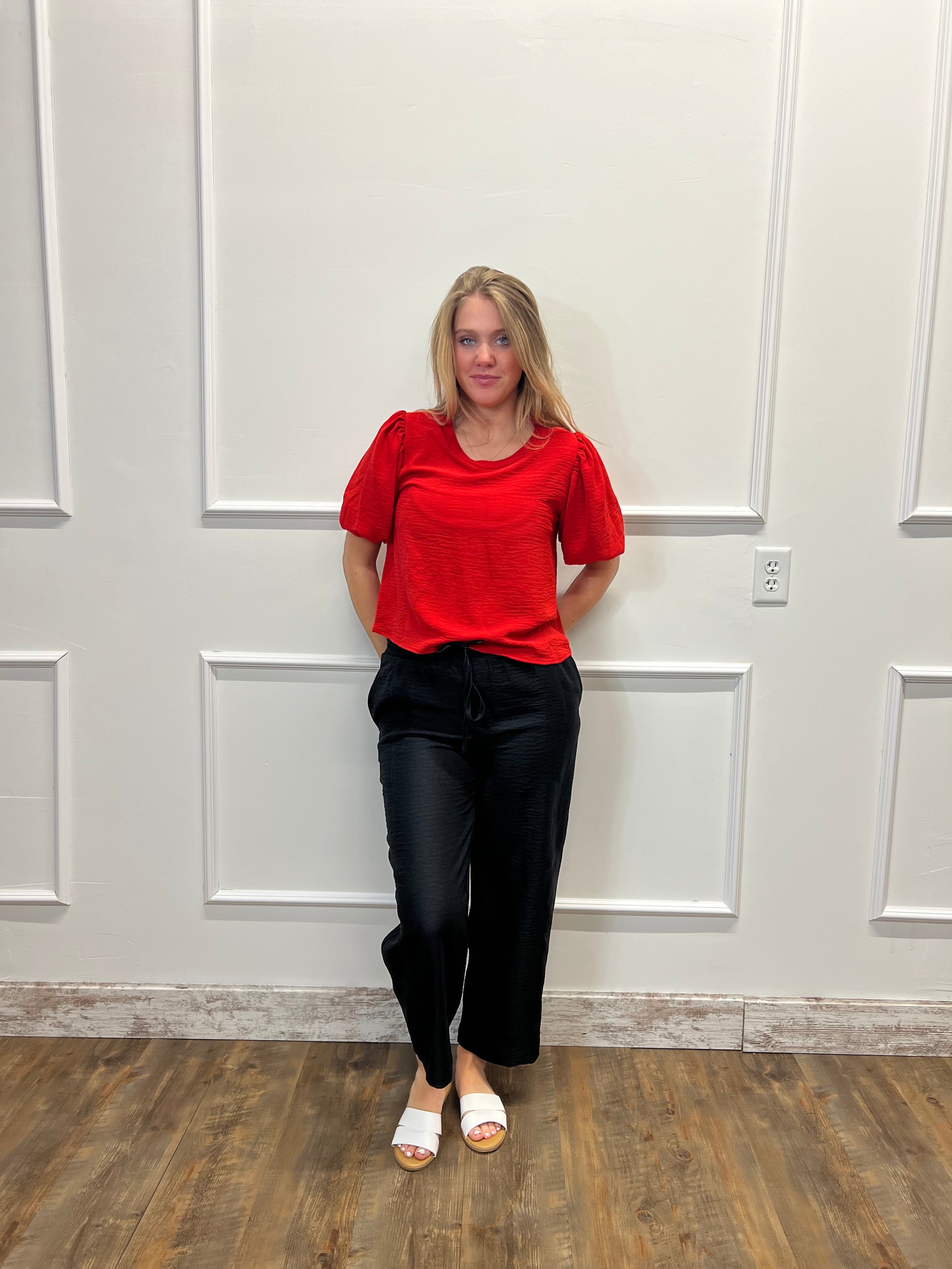 Person wearing a red top and black pants standing in front of a white door.