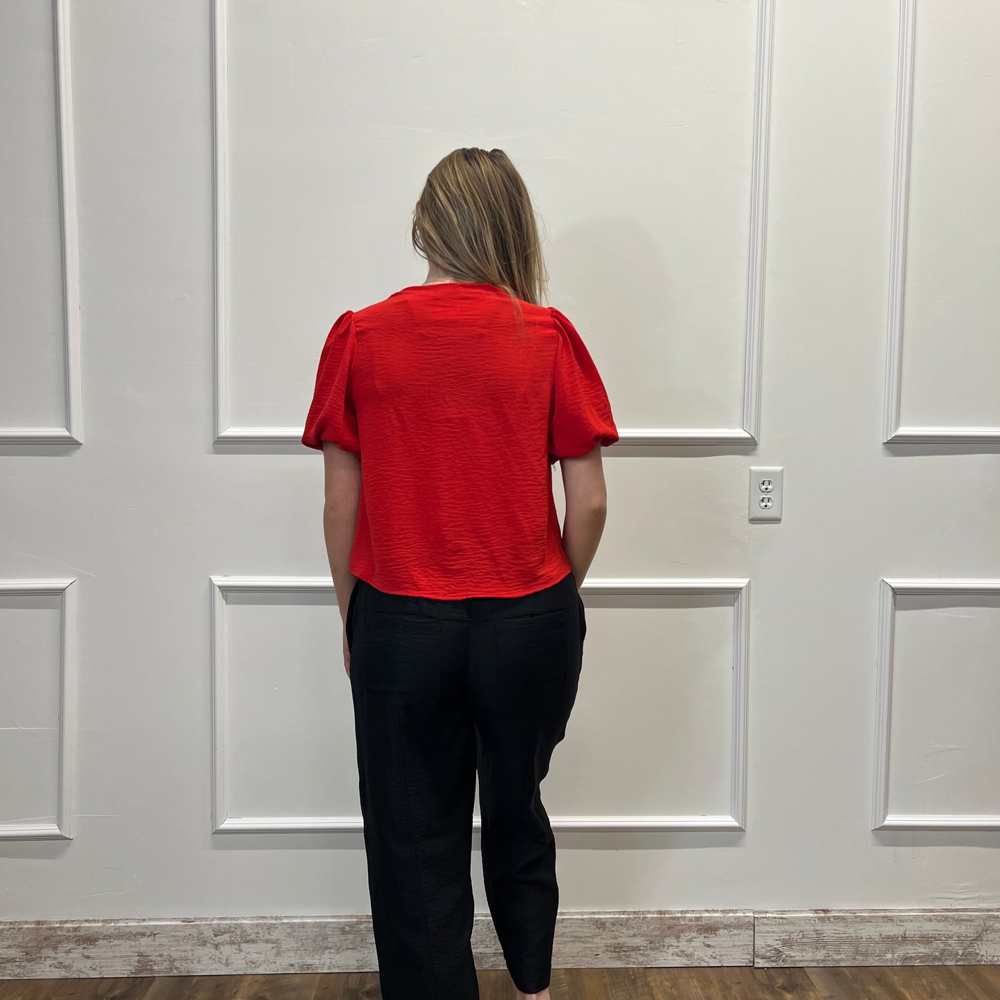 Person wearing a red hoodie and black pants standing in front of a white door.