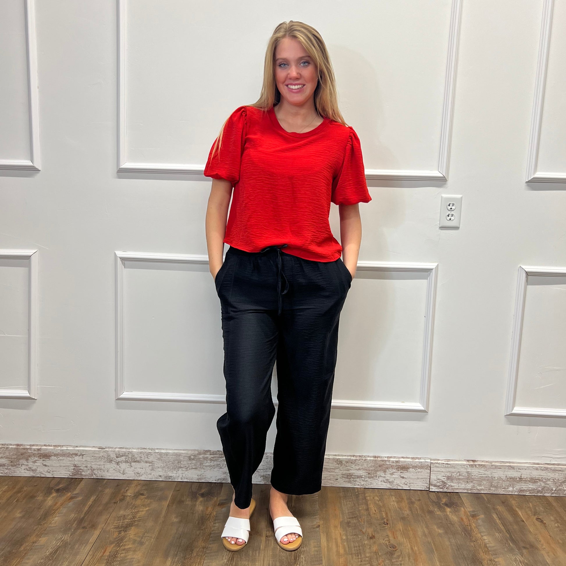 Person wearing a red top and black pants standing in front of a white door.