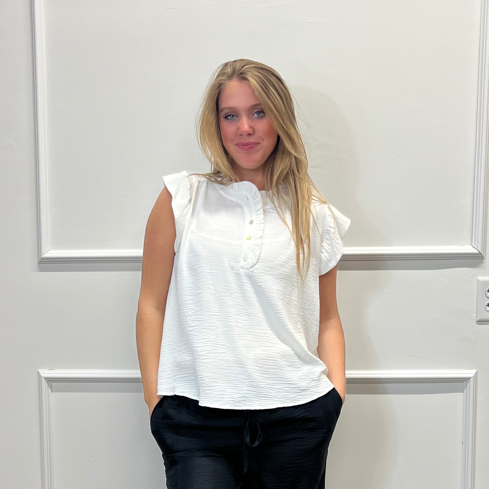 Person wearing a white shirt and black pants standing in a room with a wooden floor and white walls.