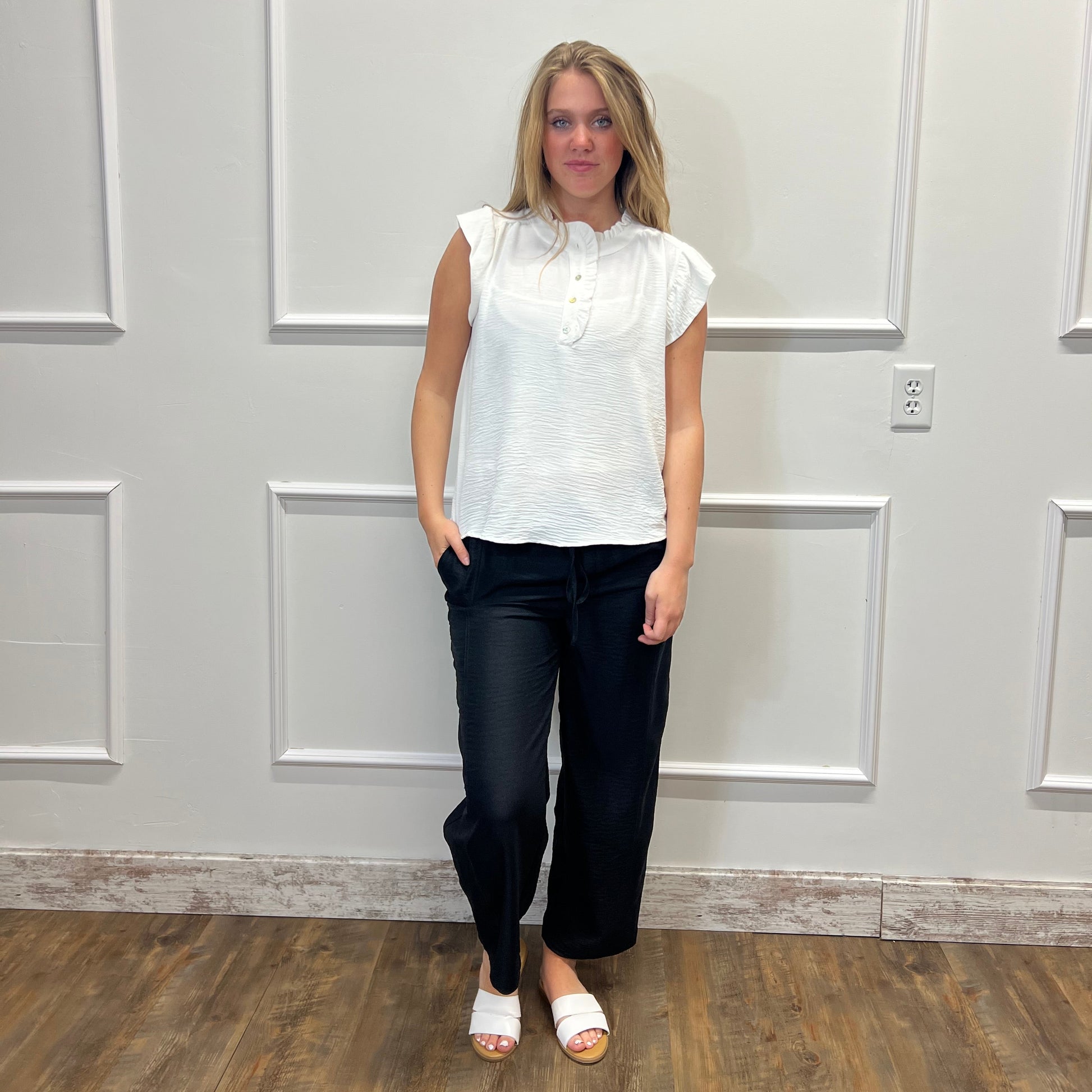 Person wearing a white blouse and black pants standing in front of a white door.