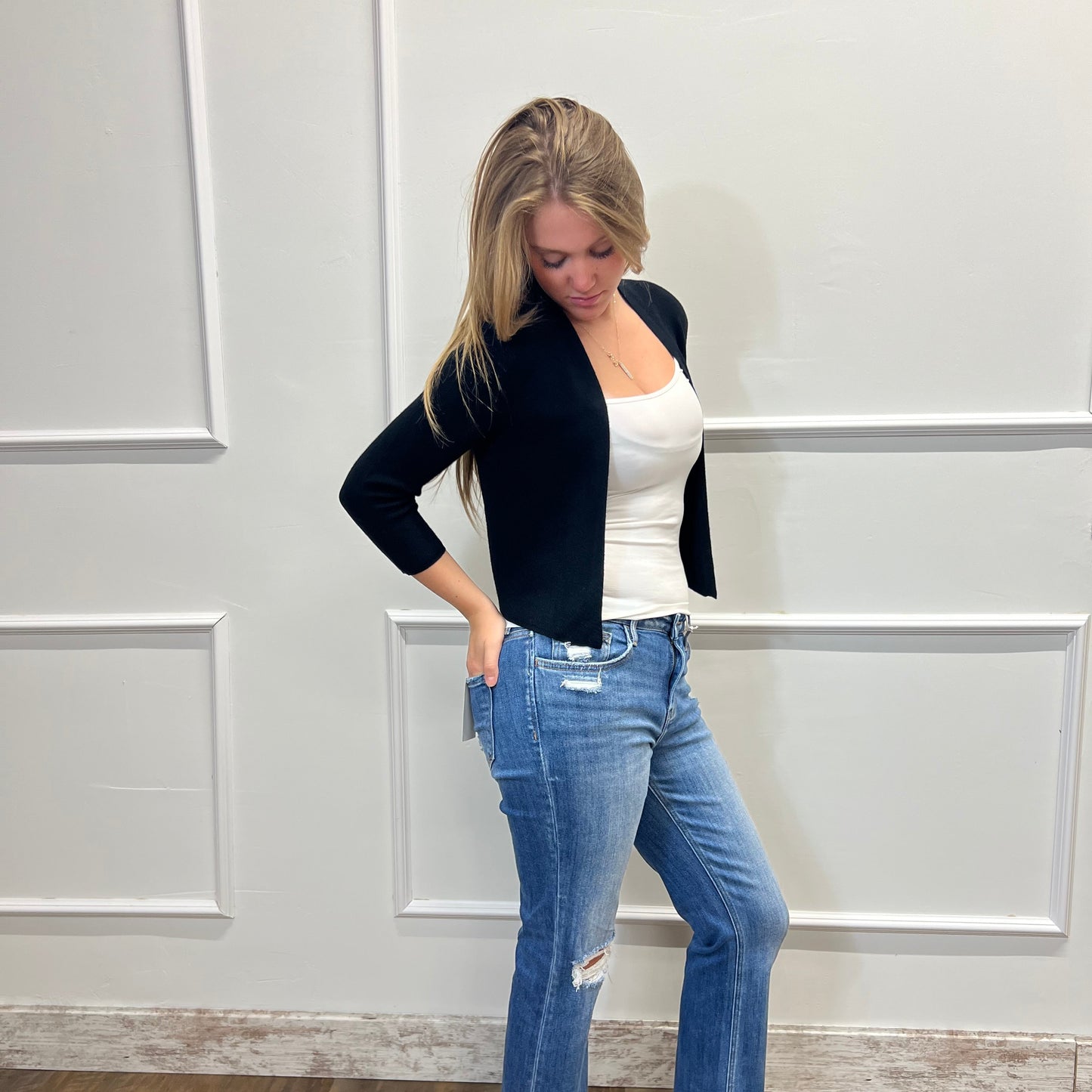 Person wearing a black top and blue jeans standing in front of a white door.