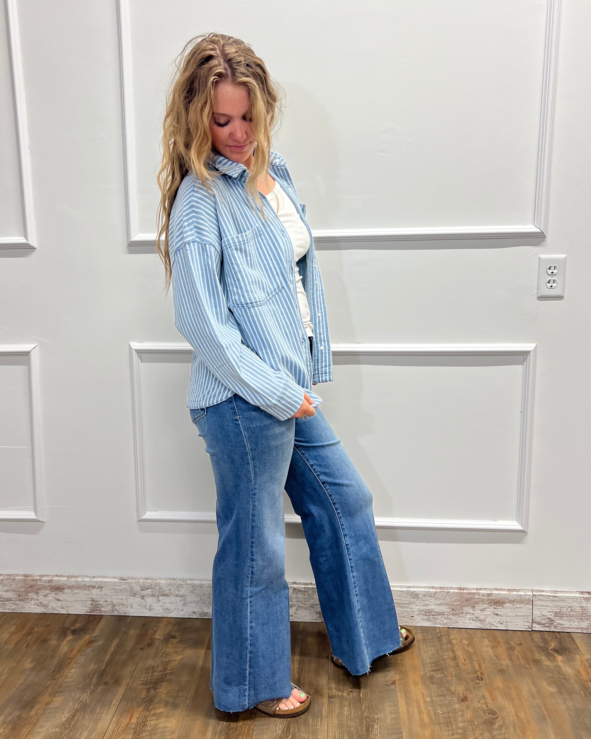 A woman takes a mirror selfie in a living room, wearing a white short-sleeve V-neck top and bright mint green skinny jeans with beige heeled sandals.