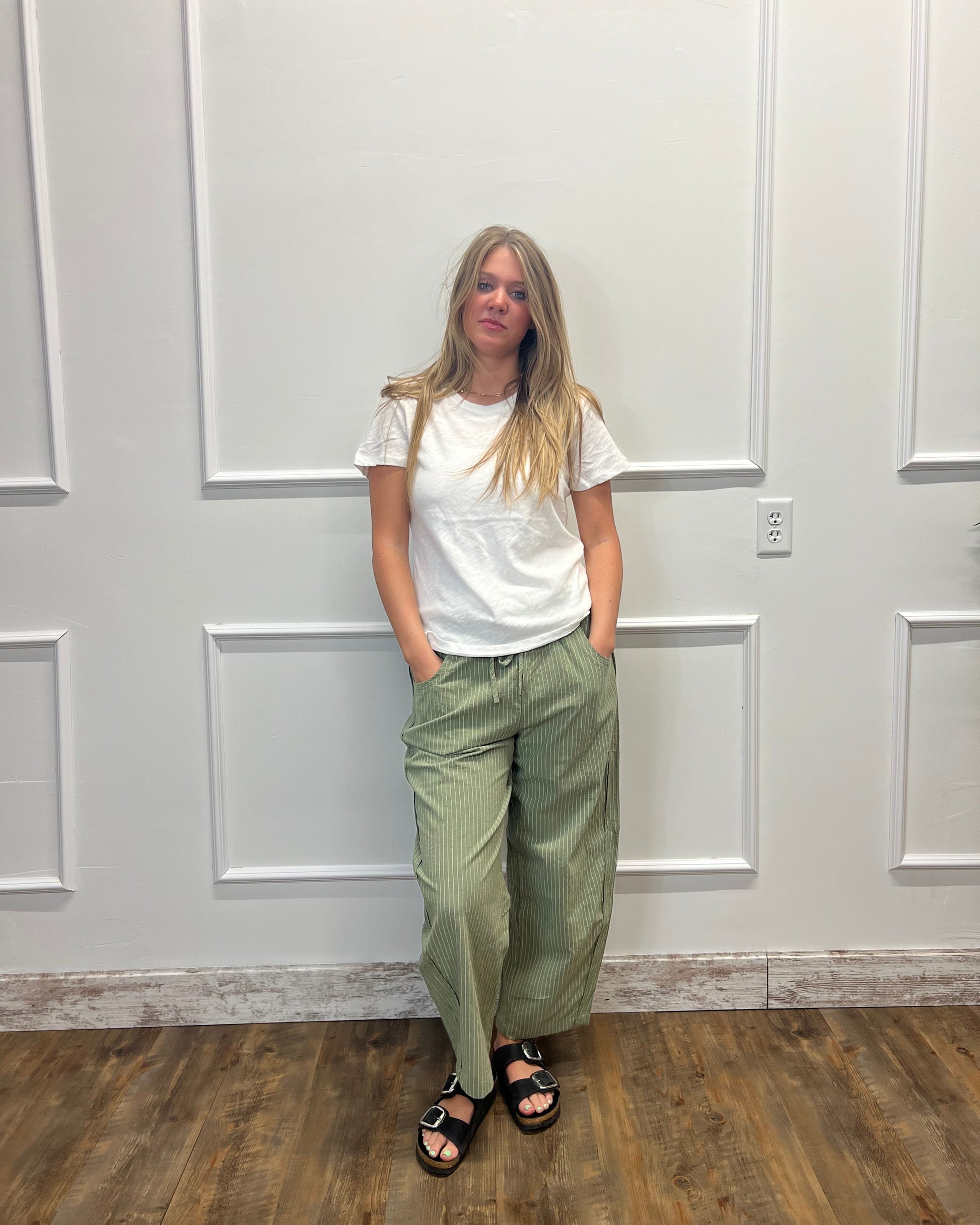 A woman wearing a white t-shirt and olive green wide-leg corduroy pants, standing in front of a white paneled door on a wood floor.