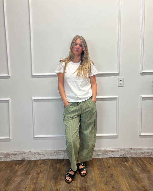 A woman wearing a white t-shirt and olive green wide-leg corduroy pants, standing in front of a white paneled door on a wood floor.