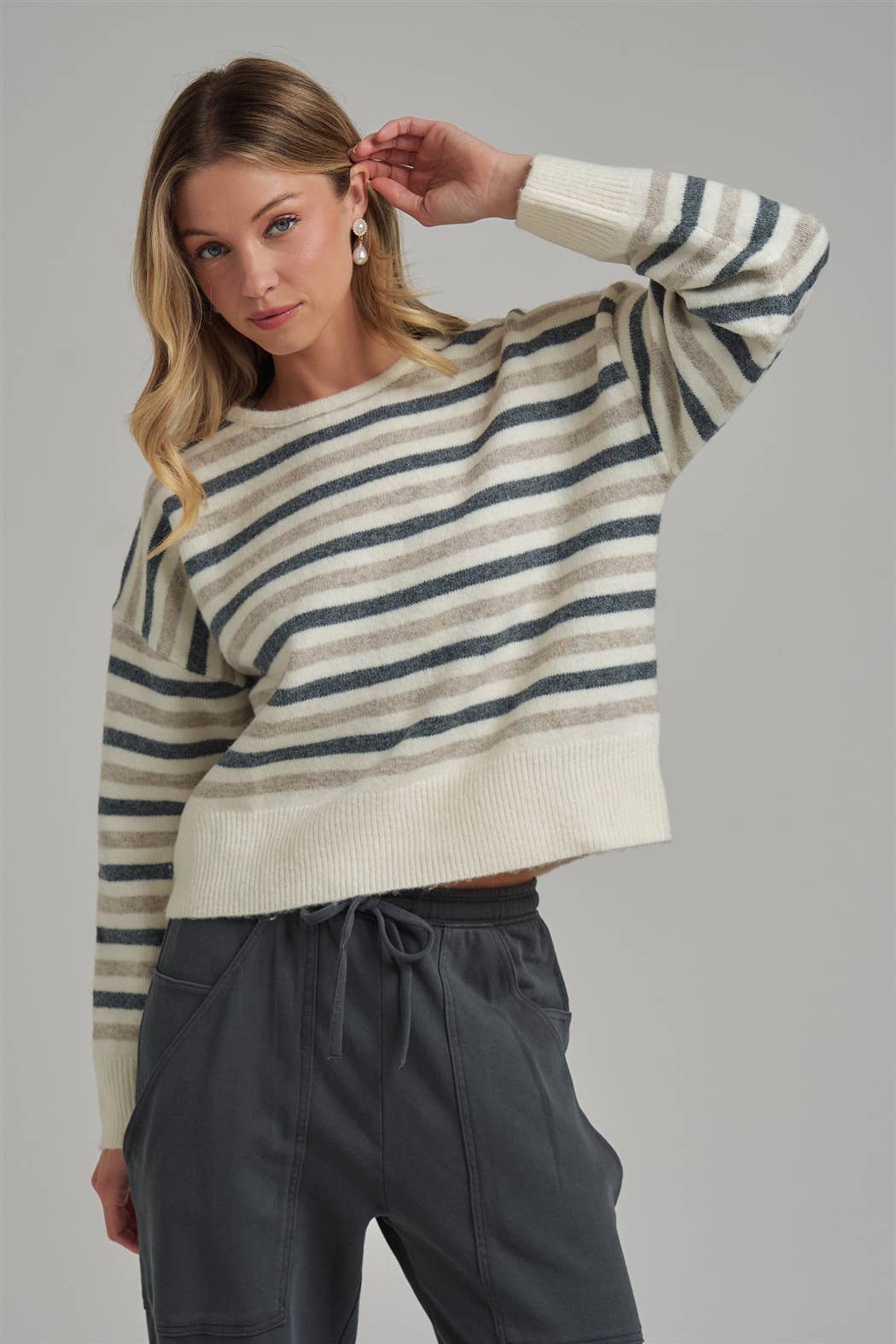 Woman wearing a striped sweater and dark pants against a gray background