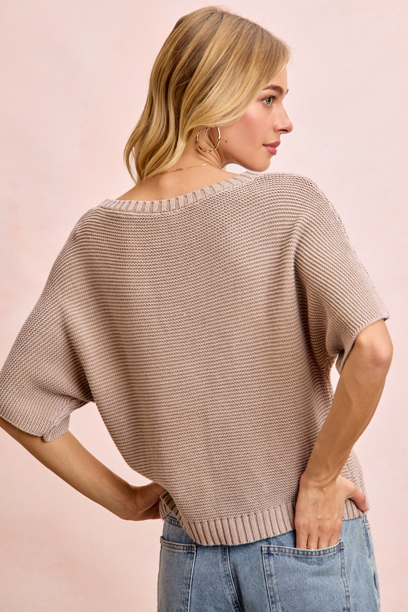 Woman wearing a beige knit sweater and blue jeans on a pink background