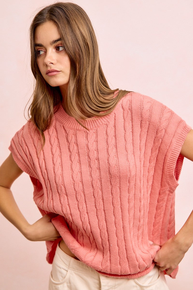 Woman wearing a pink knitted sleeveless top against a pink background