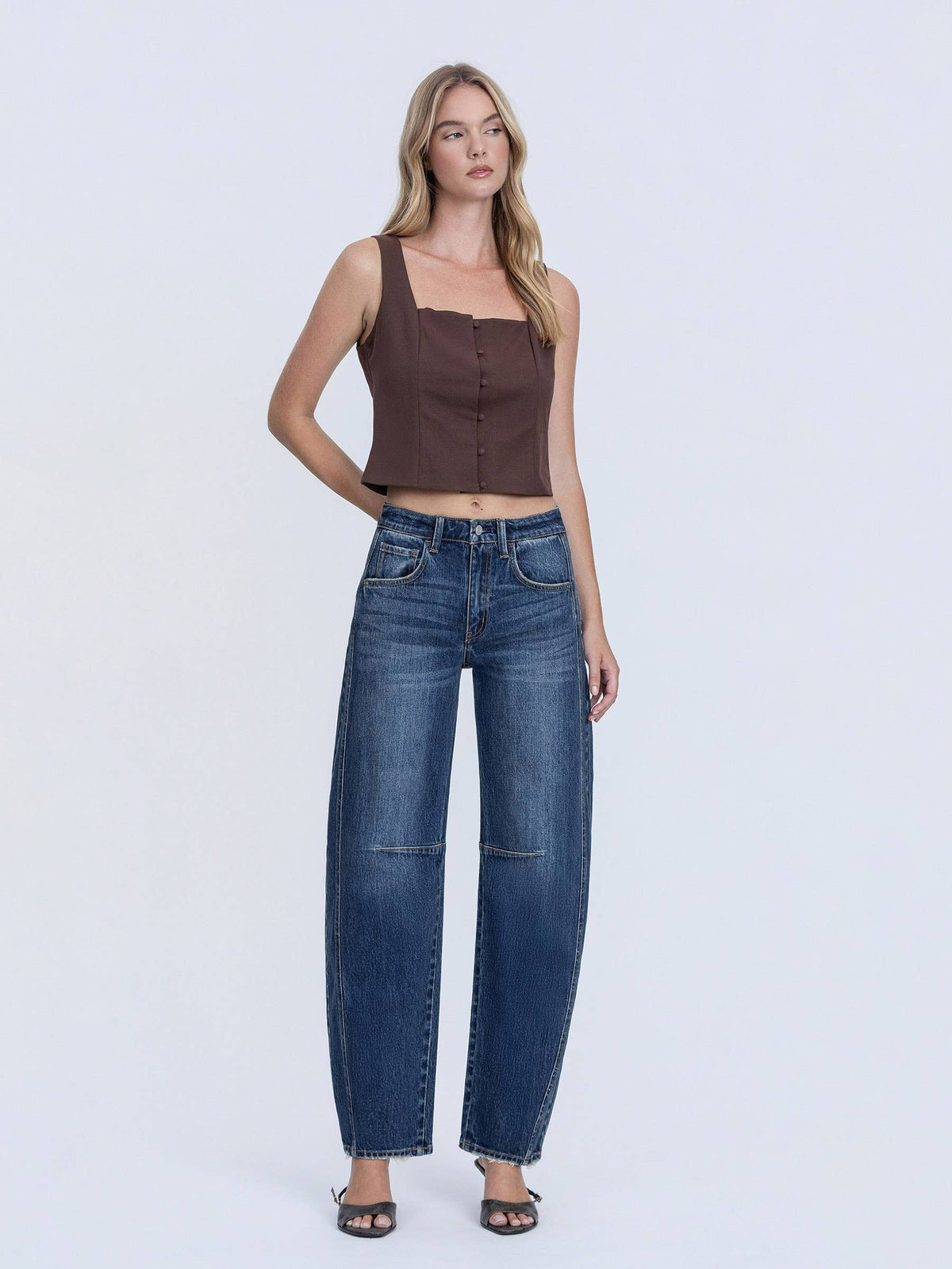 Woman wearing a brown tank top and blue jeans on a white background