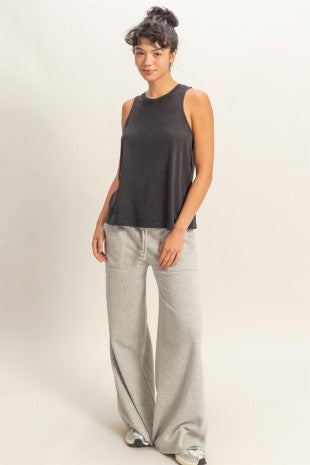 Woman wearing a black sleeveless top and light gray pants on a white background