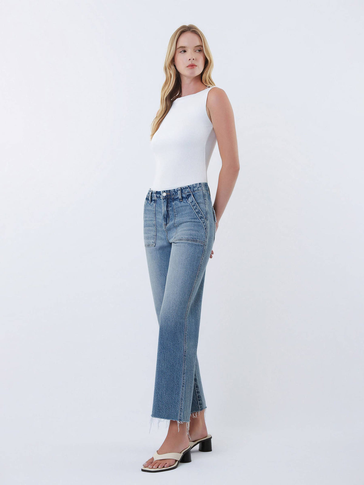 Woman wearing a white sleeveless top and blue jeans on a white background