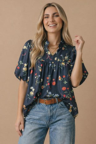 Woman wearing a navy floral blouse and blue jeans on a beige background