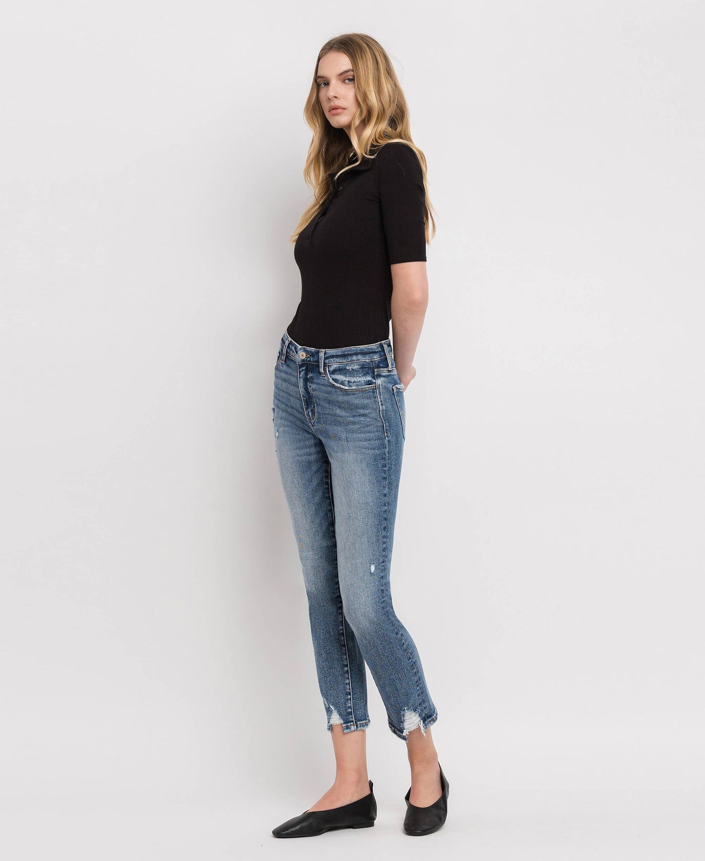 Woman wearing a black top and blue jeans against a white background