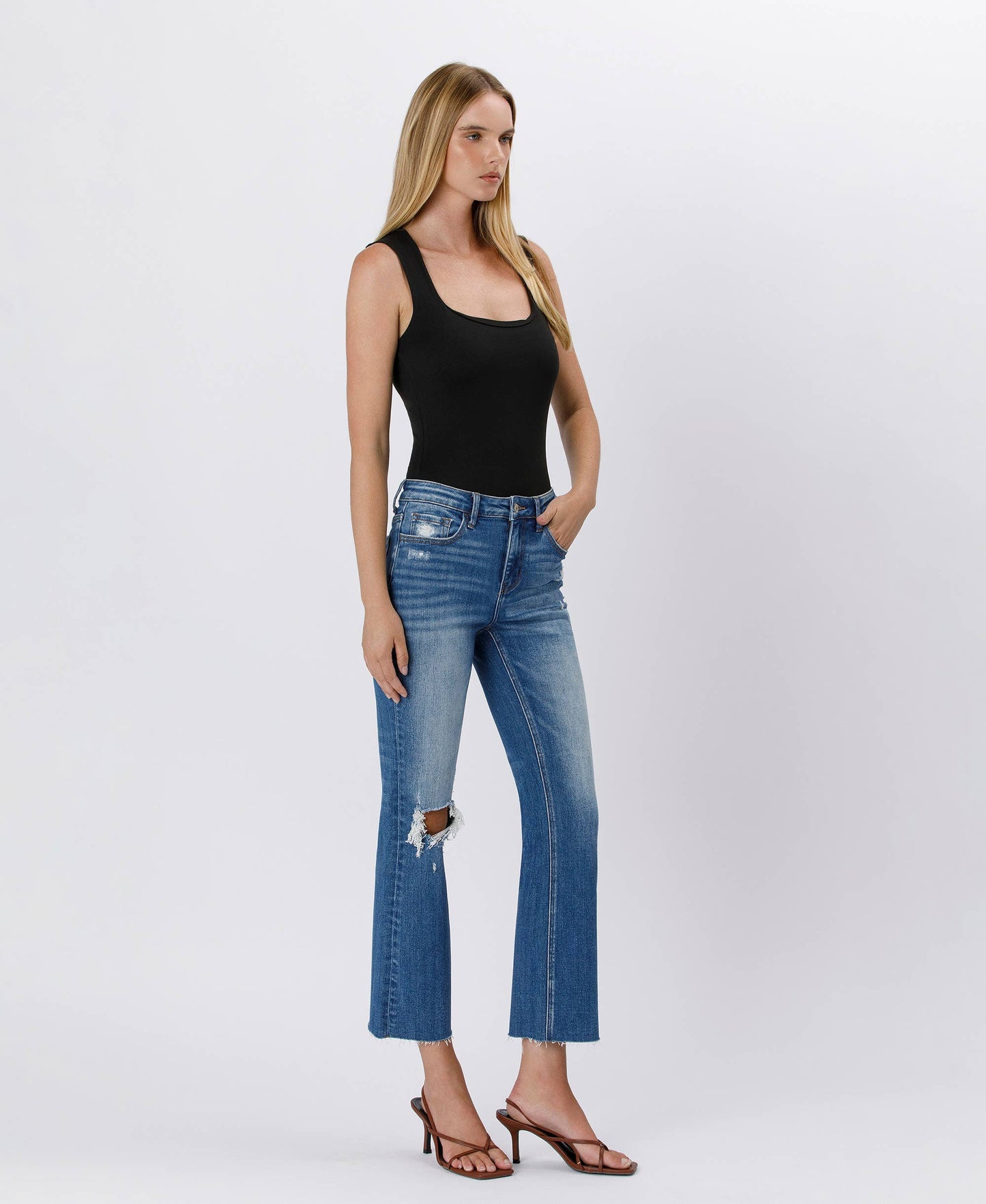 Woman wearing blue jeans and a black tank top on a white background