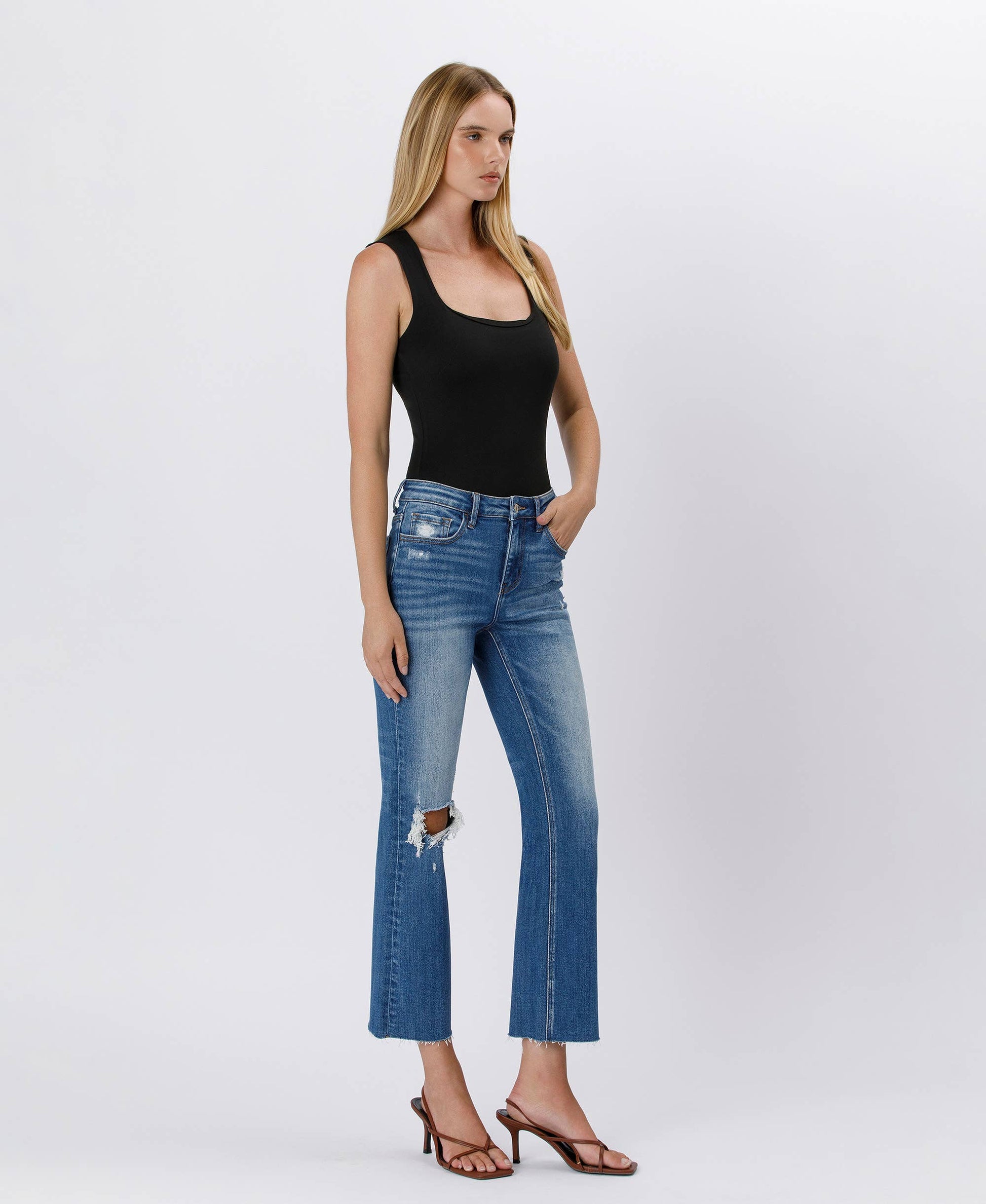 Woman wearing blue jeans and a black tank top on a white background