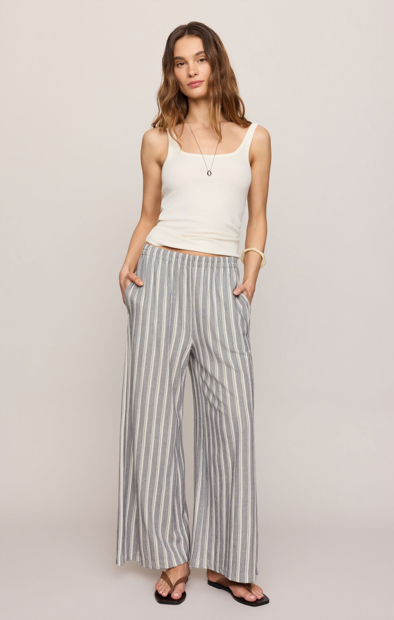 Woman wearing a white tank top and striped pants on a plain background