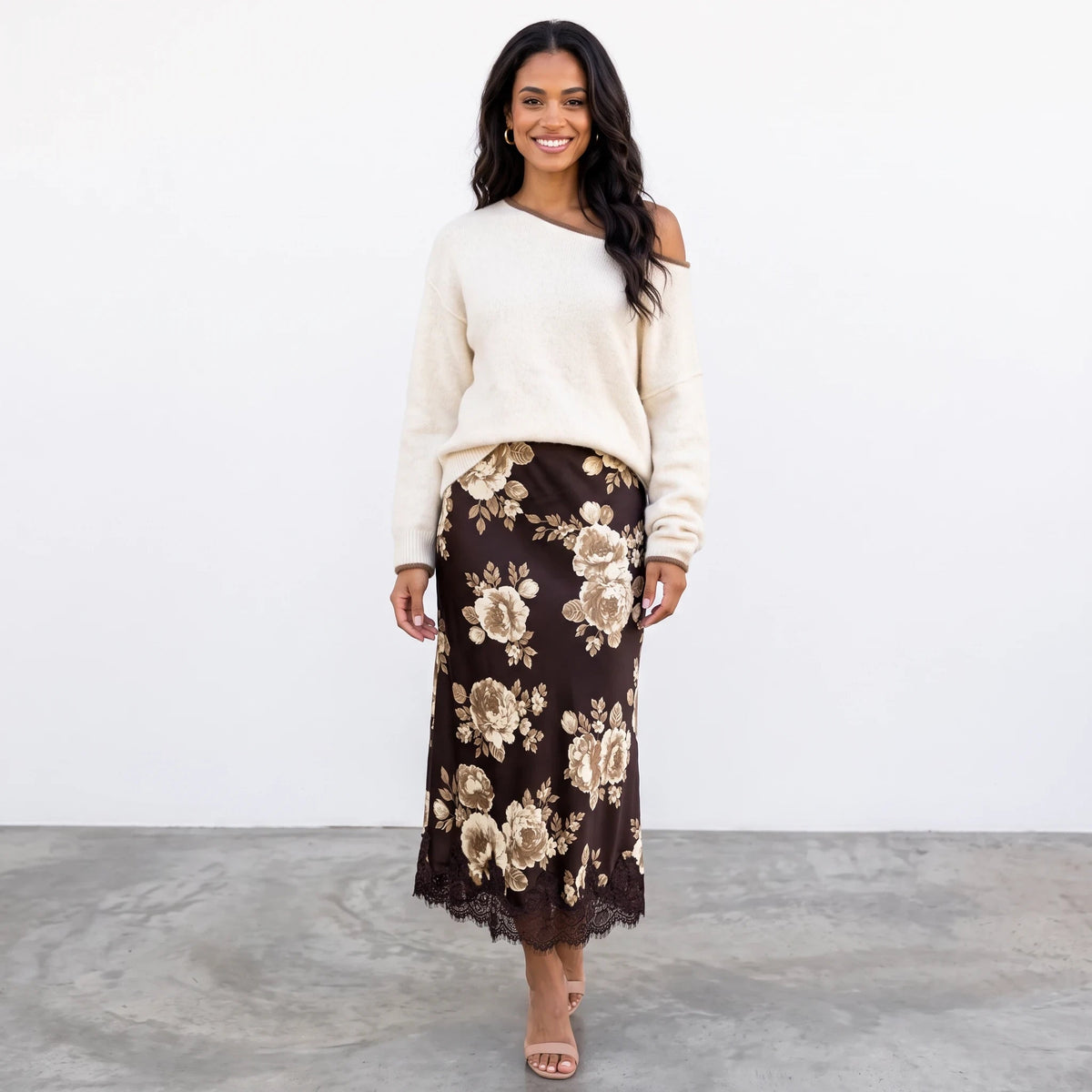 A smiling model wears the Apricot Lane Duluth Autumn Glow Sweater in cream with a brown floral midi skirt and heels.