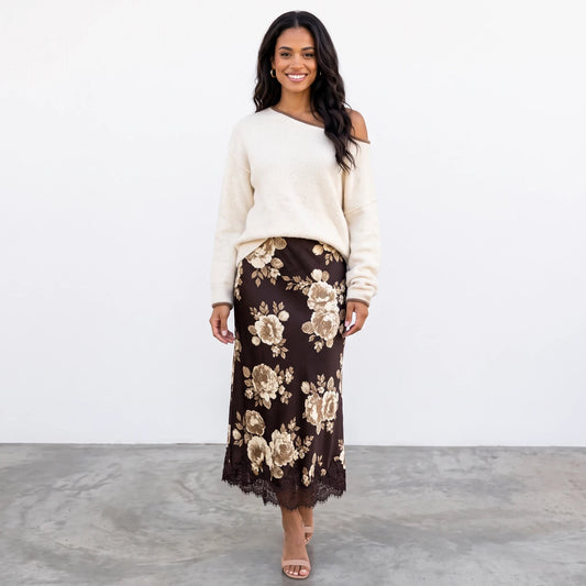 A smiling model wears the Apricot Lane Duluth Autumn Glow Sweater in cream with a brown floral midi skirt and heels.