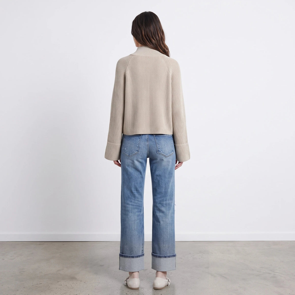 Back view of a woman wearing the Apricot Lane Duluth Avery beige textured zip-up knit cardigan with cuffed jeans.