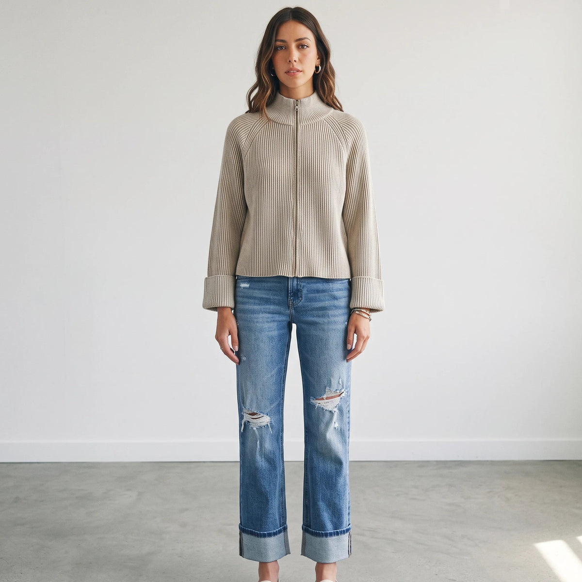 Model wearing Apricot Lane Duluth beige textured zip-up knit cardigan with long sleeves and blue distressed denim jeans