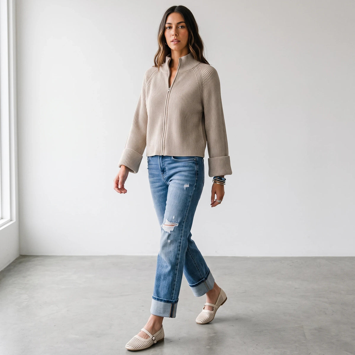 Model wearing Apricot Lane Duluth beige textured zip-up knit cardigan with cuffed sleeves, jeans, and flats.
