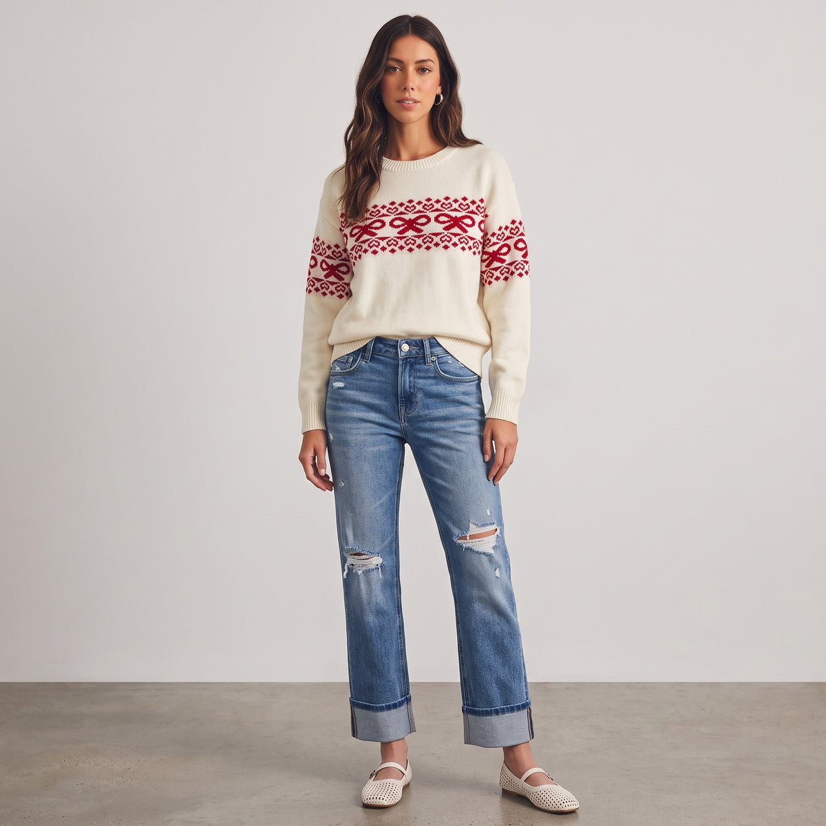 Model wearing Apricot Lane Duluth cream sweater with red bow and heart Fair Isle pattern and distressed blue jeans