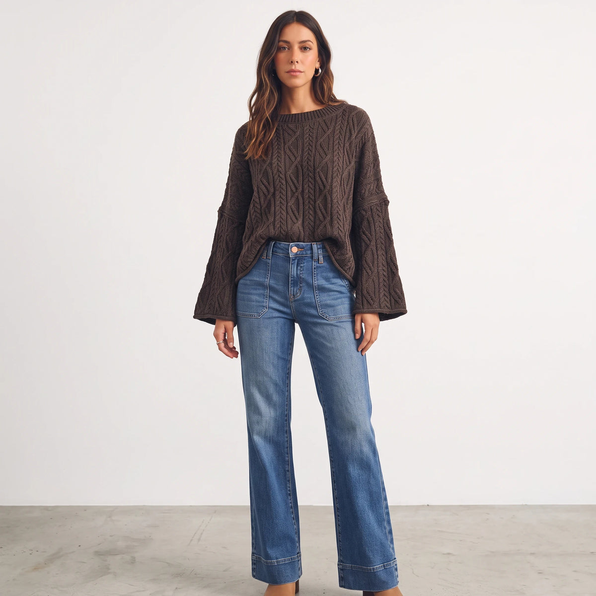 Model wearing The Isla oversized brown cable knit sweater with wide sleeves, styled with blue flare denim jeans.