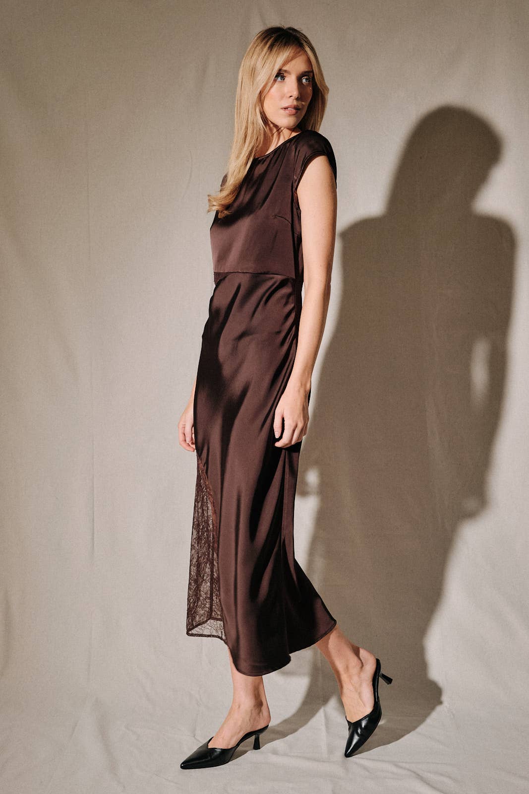 Model wearing Apricot Lane Duluth brown satin midi dress with cap sleeves and sheer lace side inserts