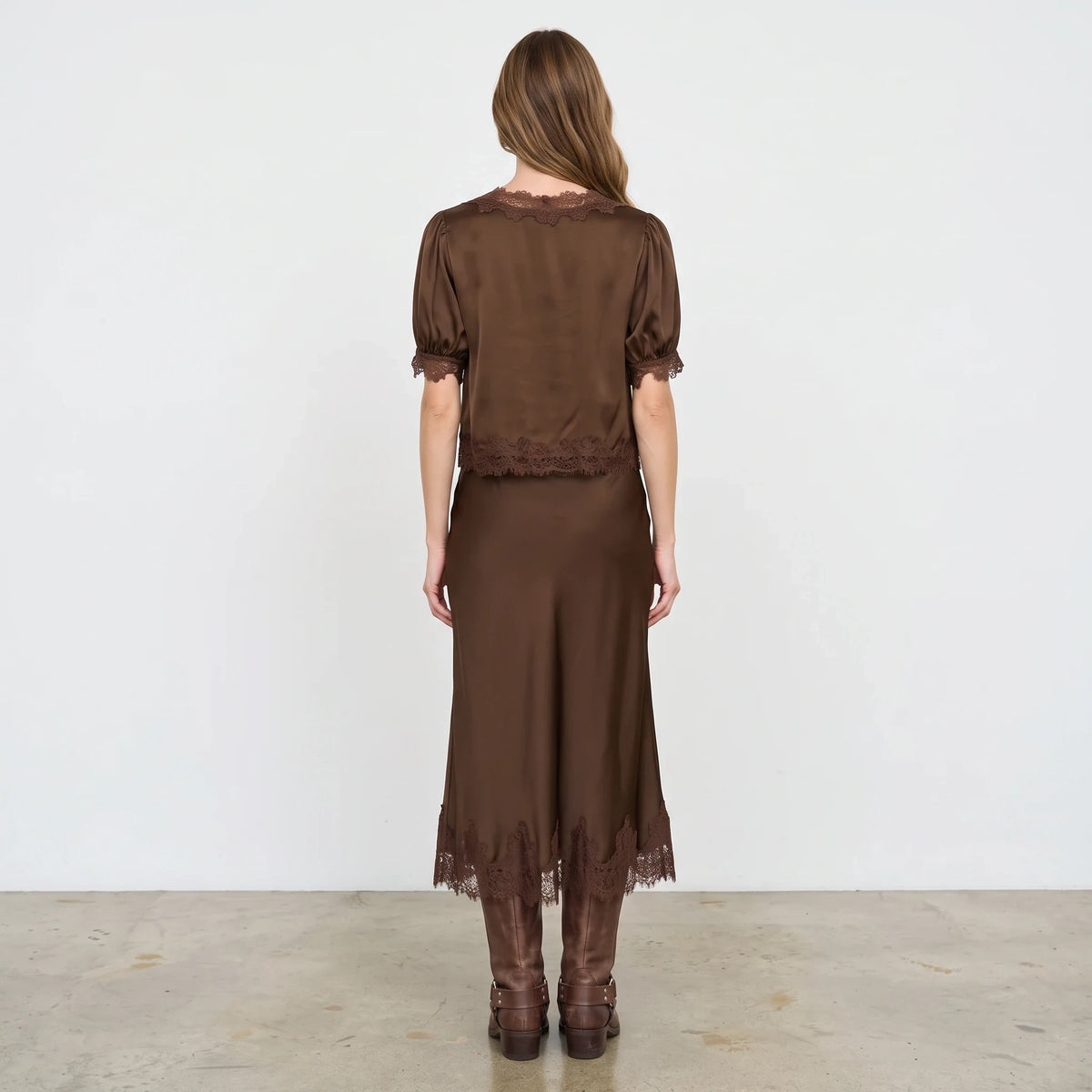 Model wearing Apricot Lane Duluth brown satin skirt and matching top with delicate lace hem detail and tall boots
