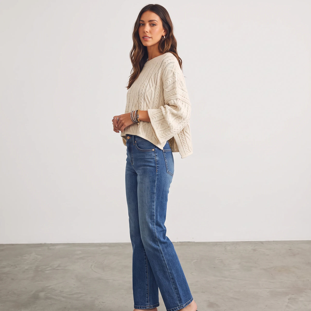 Model wearing an Apricot Lane Duluth cream oversized cable knit sweater with long sleeves and blue denim jeans