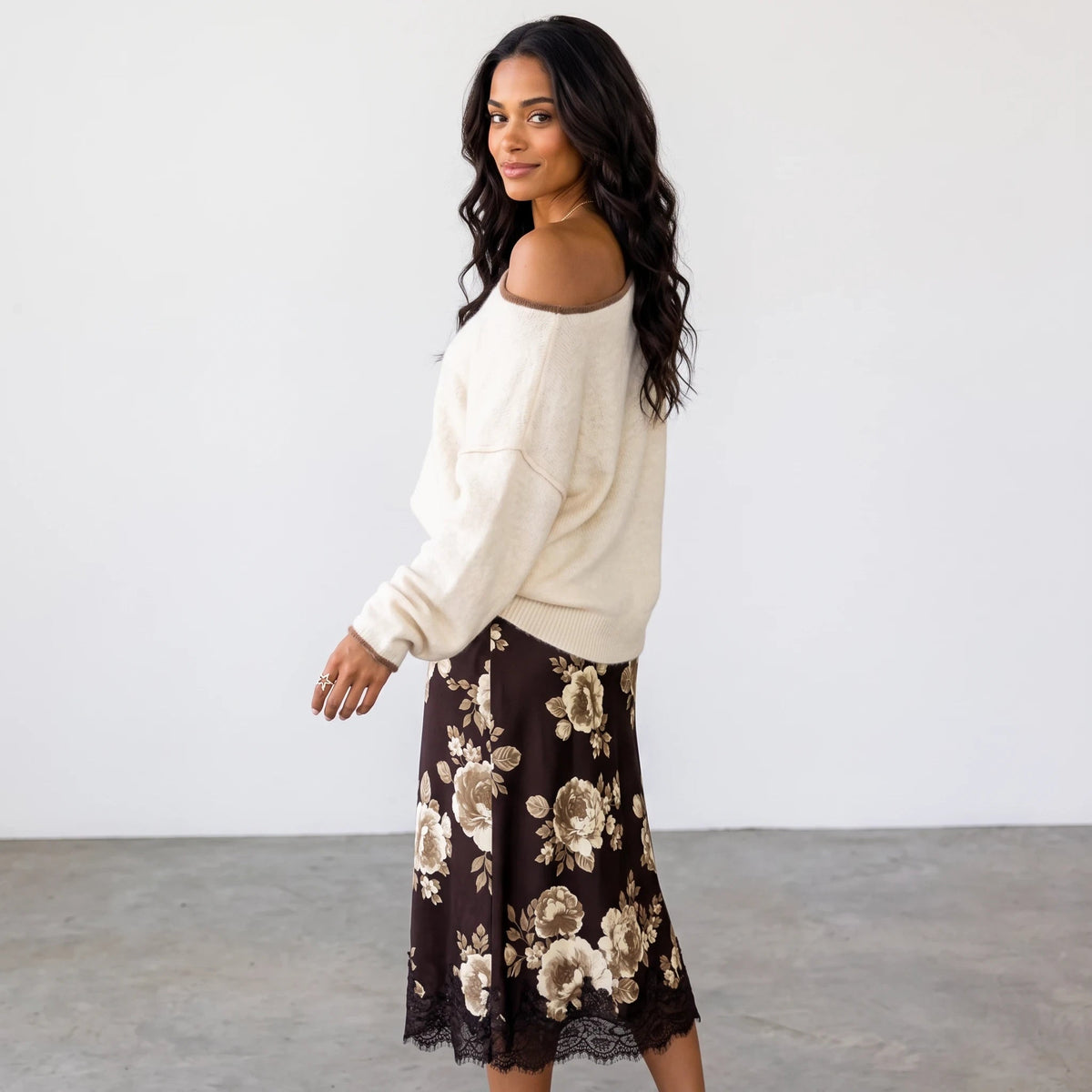 Model wearing Apricot Lane Duluth Autumn Glow Sweater in cream paired with a floral midi skirt against white wall