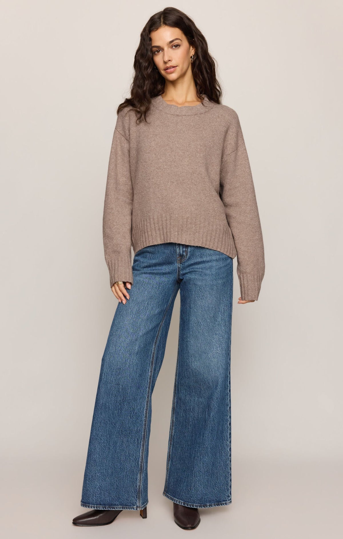Model wearing Apricot Lane Duluth Easton pullover sweater in taupe with crew neck and wide-leg blue jeans