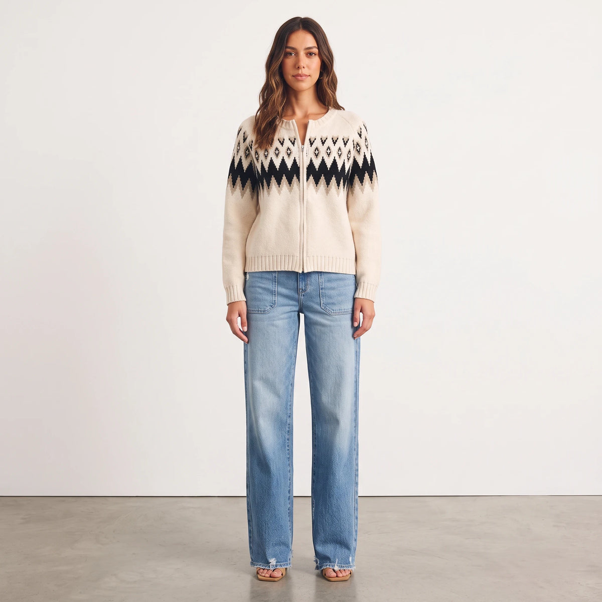 Model wearing Apricot Lane Duluth Aspen Fair Isle zip-front cardigan in cream and black with blue denim jeans