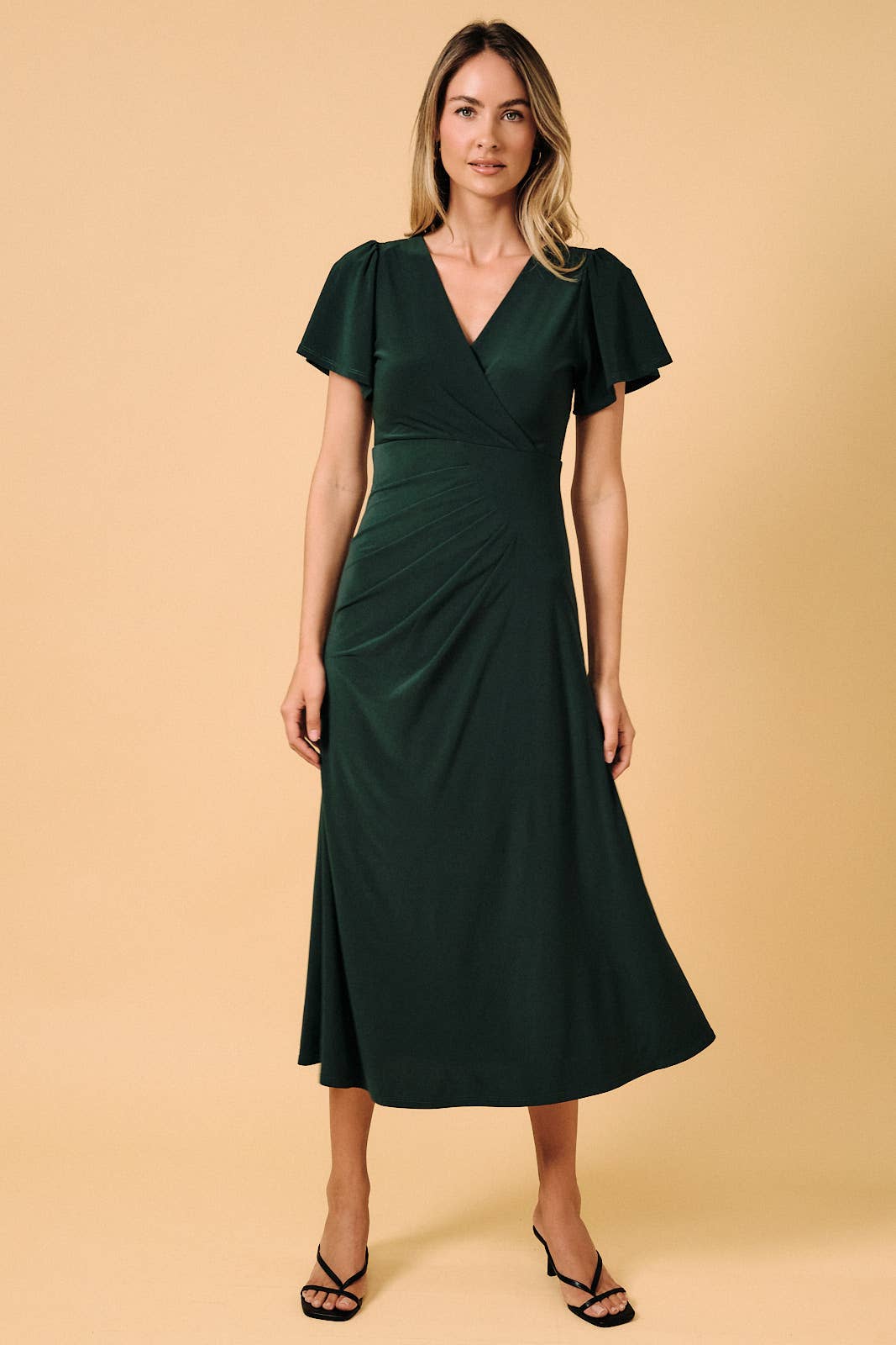 Model wearing an Apricot Lane Duluth dark green midi dress with a surplice V-neck, flutter sleeves, and side pleats.