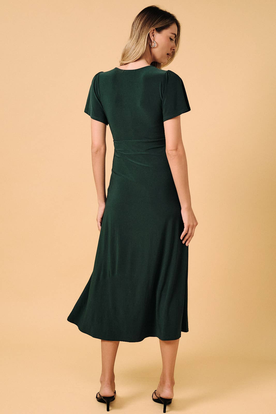 Back view of a woman wearing an Apricot Lane Duluth dark green midi dress with flutter sleeves and pleated detail