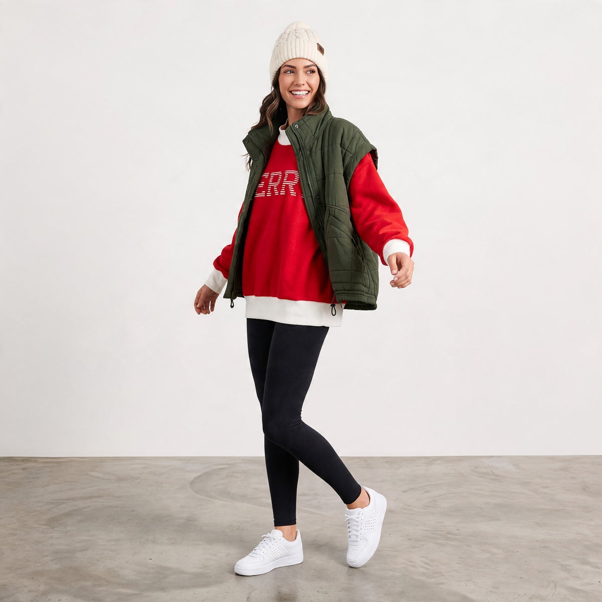 Apricot Lane Duluth model wearing a green puffer vest over a red sweatshirt, black leggings, and a white beanie.