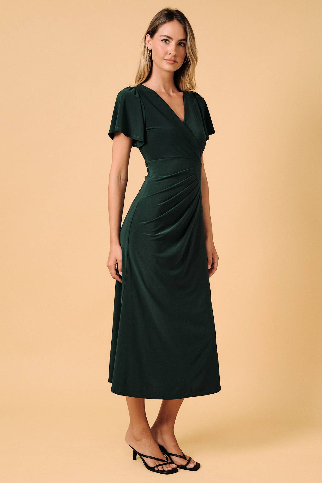 Model wearing an Apricot Lane Duluth dark green midi dress with a surplice V-neck, flutter sleeves, and pleating.