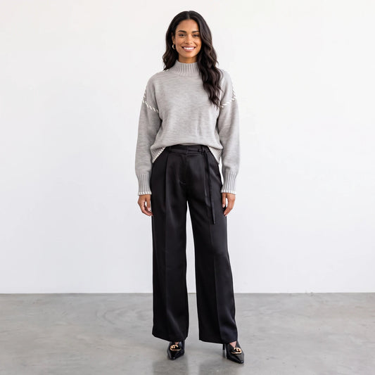 Model wearing Apricot Lane Duluth grey turtleneck sweater with stitch detail, paired with black wide-leg trousers.