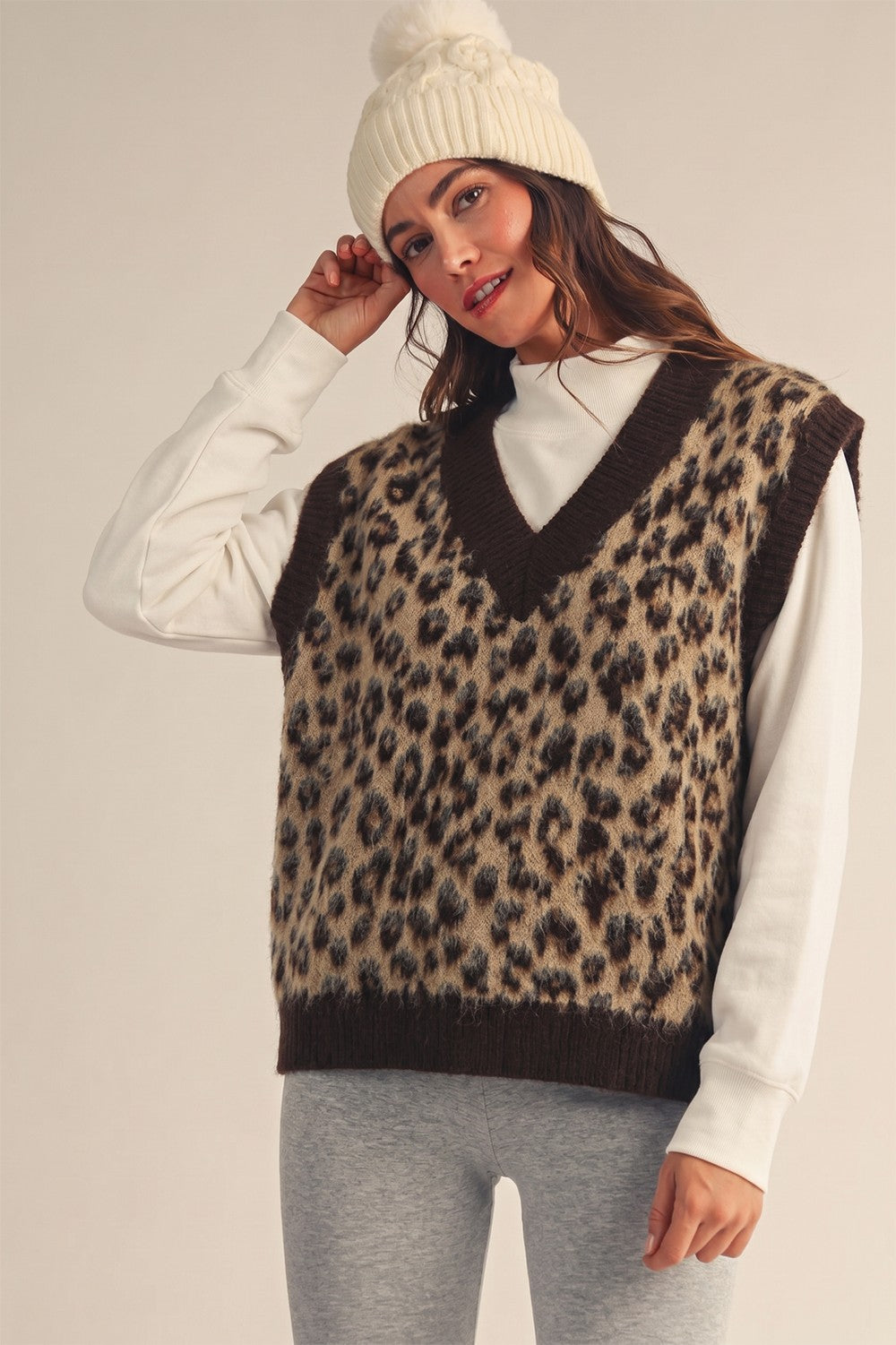Model wearing Apricot Lane Duluth leopard print fuzzy sweater vest over a white long-sleeve top and cream beanie