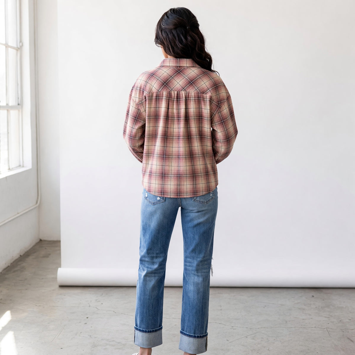 Back view of a woman wearing the Apricot Lane Duluth Maren plaid shirt with blue cuffed jeans in a studio setting.