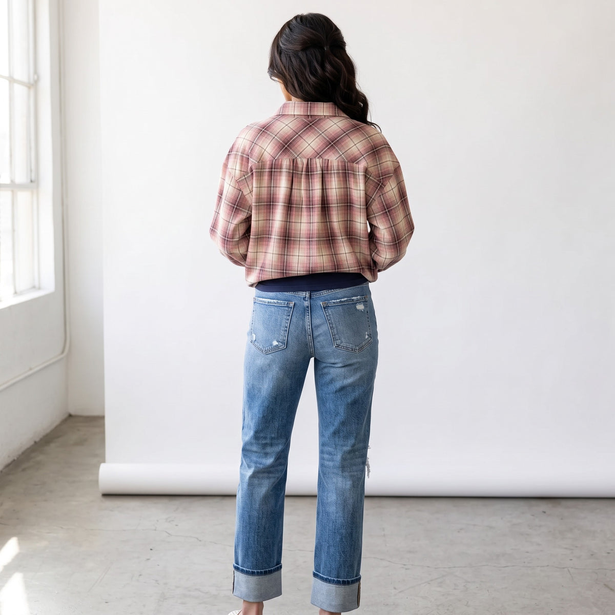 Back view of a woman wearing the Apricot Lane Duluth Maren plaid shirt in muted pink and tan tones with blue jeans.