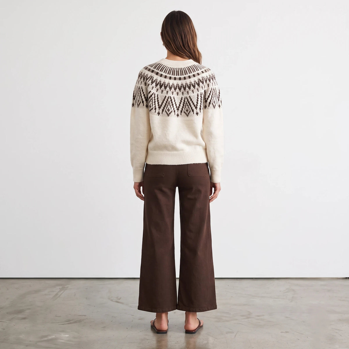 Back view of a woman wearing an Apricot Lane Duluth Margot Fair Isle sweater with a geometric yoke and brown trousers.
