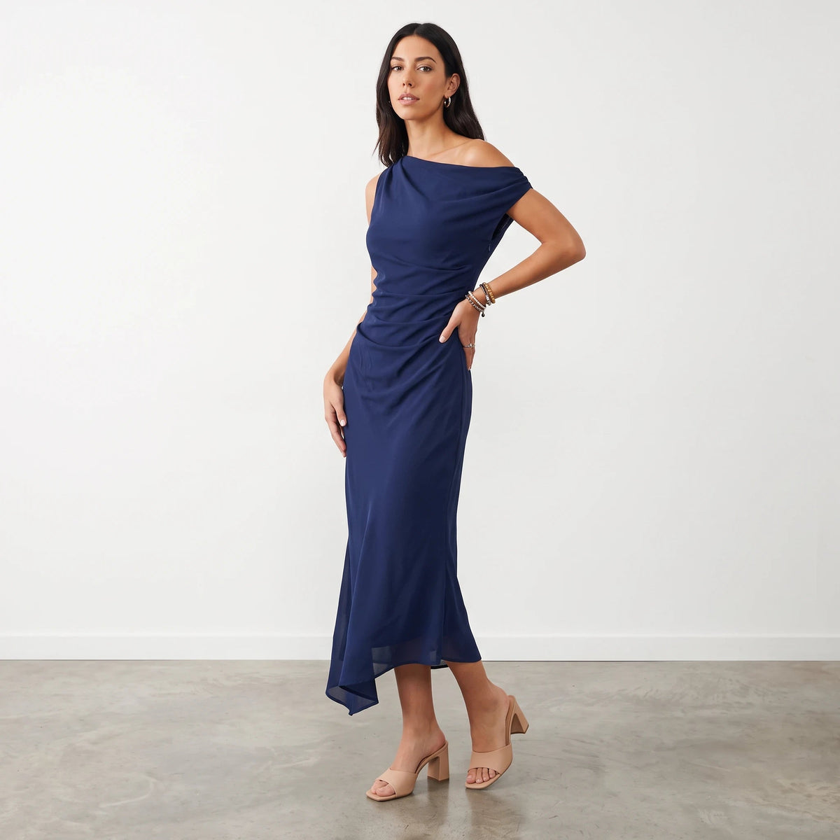 Model wearing Apricot Lane Duluth navy one-shoulder midi dress in crepe fabric with a draped back and sheath fit.
