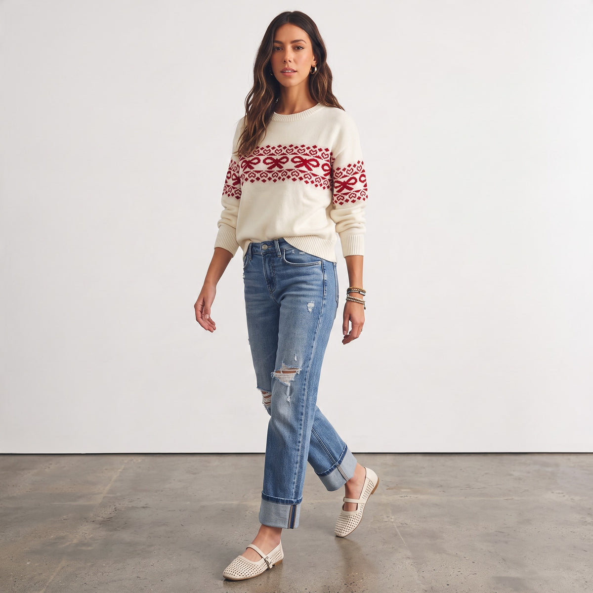 Model wearing Apricot Lane Duluth cream sweater with red bow and heart Fair Isle pattern, styled with distressed jeans