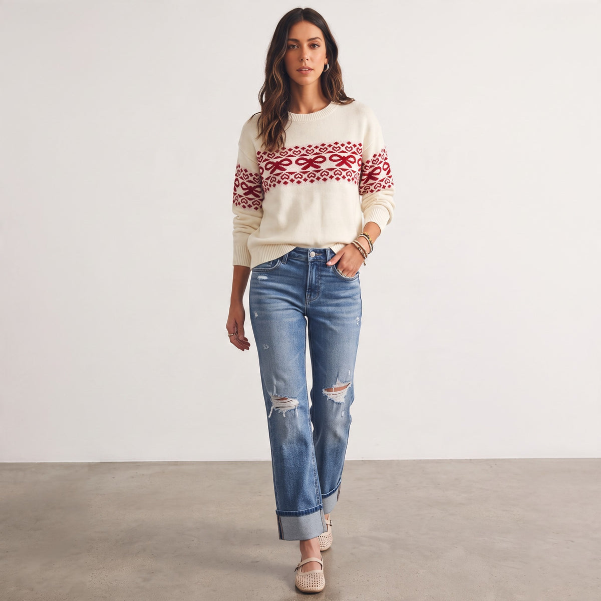 Model wearing Apricot Lane Duluth Noelle cream sweater with red bow and heart Fair Isle pattern and distressed jeans