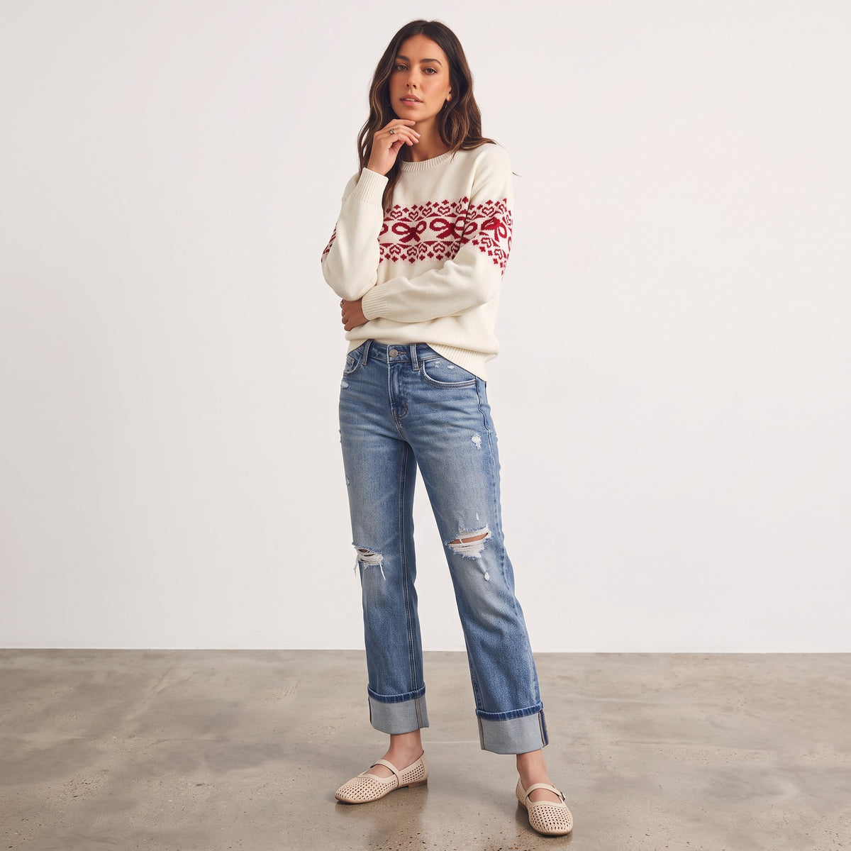 Model wearing Apricot Lane Duluth Noelle Bow Fair Isle sweater with red heart and bow motifs and blue distressed jeans