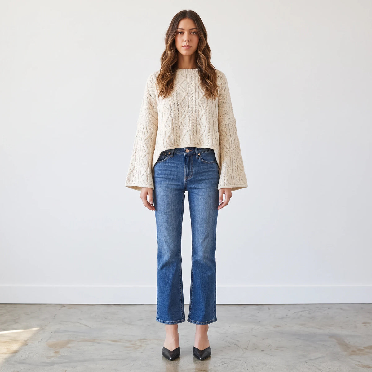 Model wearing Apricot Lane Duluth oversized cream cable knit sweater with flared sleeves and blue denim jeans