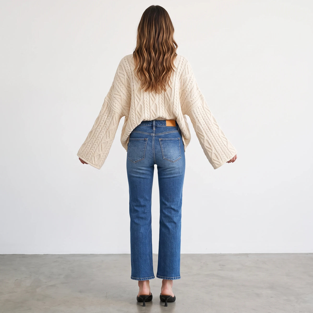 Back view of a woman wearing the Apricot Lane Duluth Isla oversized cream cable knit sweater with blue denim jeans.